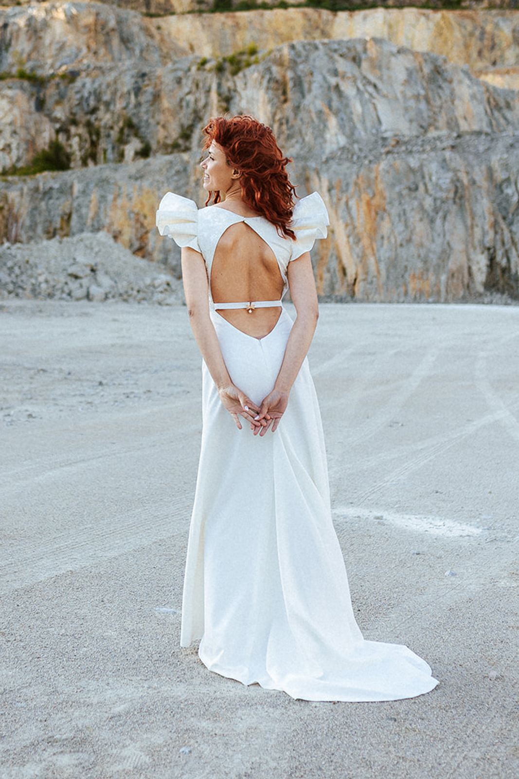 Femme rousse portant une robe de mariée à épaulettes de créateur en dentelle sur-mesure.