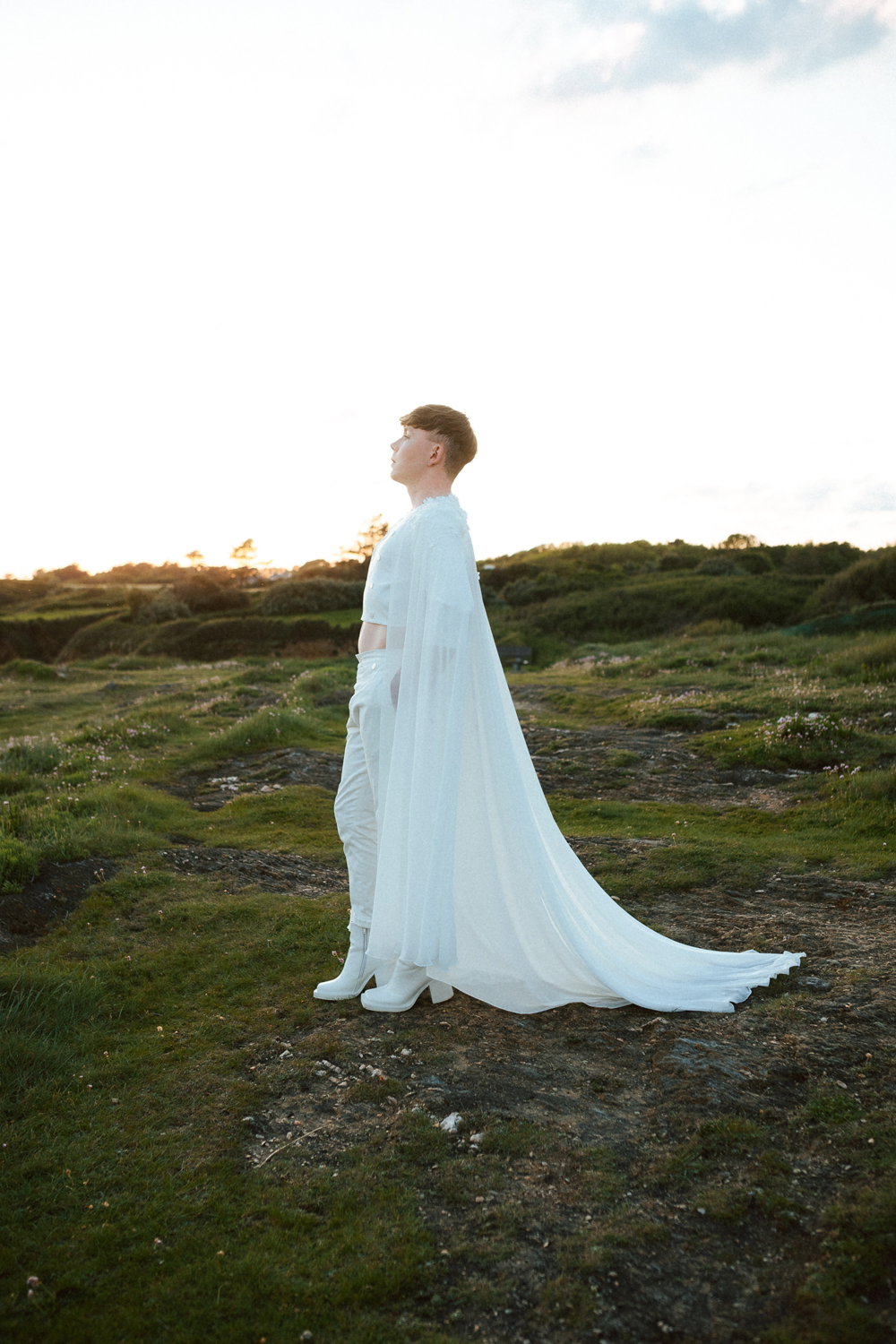Homme portant un costume de mariage avec une cape en dentelle sur-mesure en bord de mer.