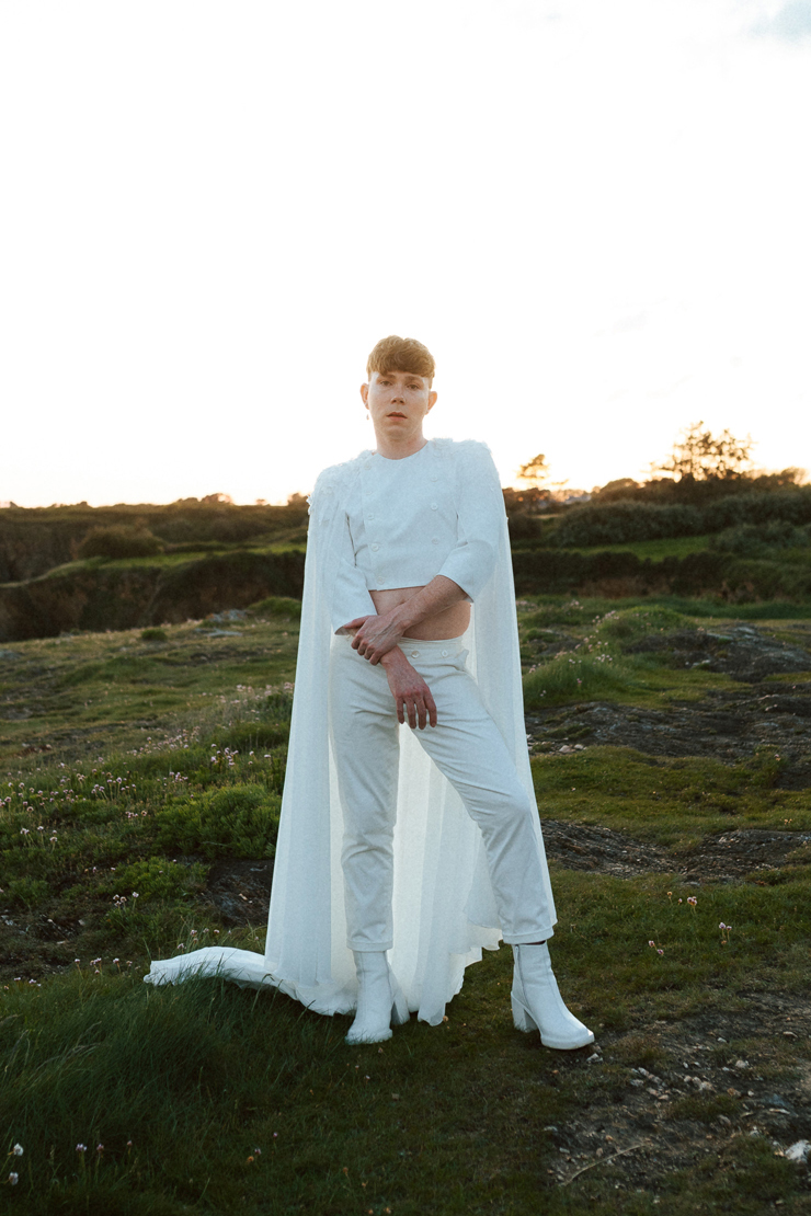 Homme portant un costume de mariage avec une cape en dentelle sur-mesure en bord de mer.