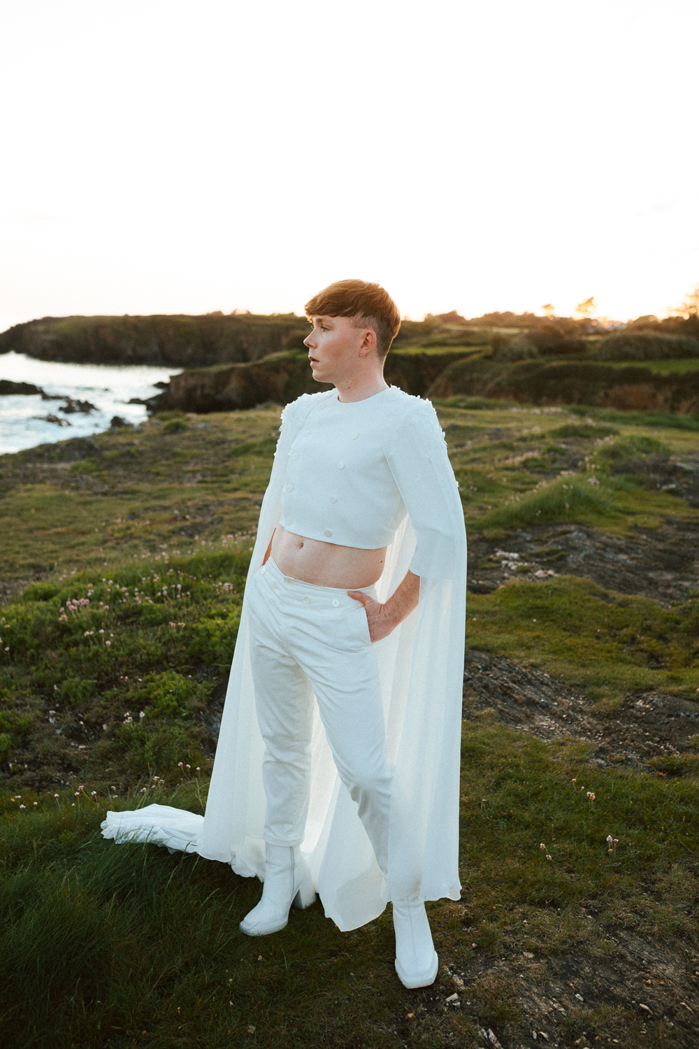 Homme portant un costume de mariage avec une cape en dentelle sur-mesure en bord de mer.