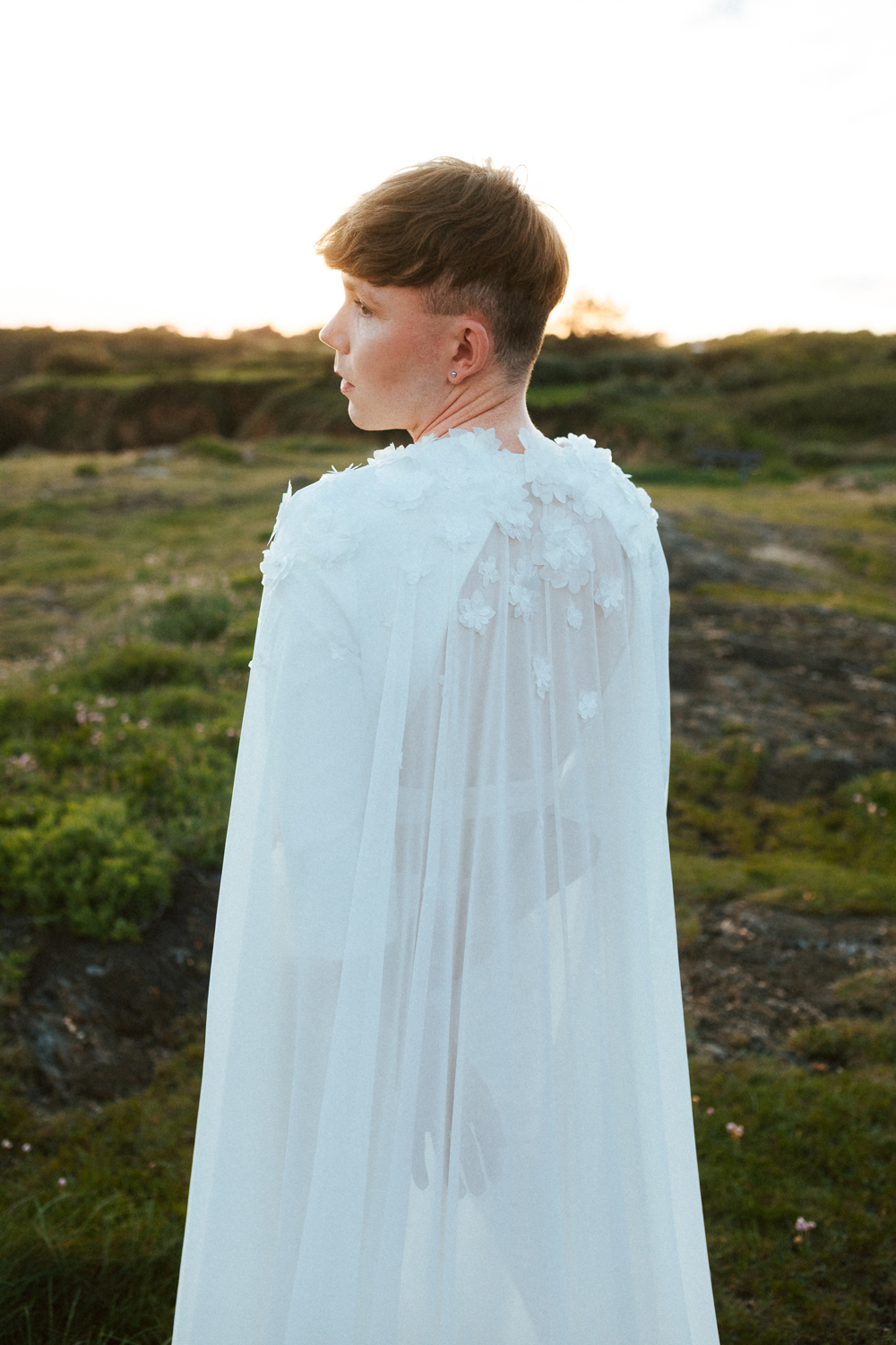 Homme portant un costume de mariage avec une cape en dentelle sur-mesure en bord de mer.