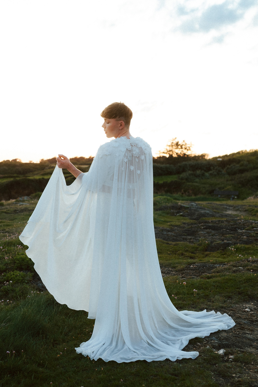 Homme portant un costume de mariage avec une cape en dentelle sur-mesure en bord de mer.