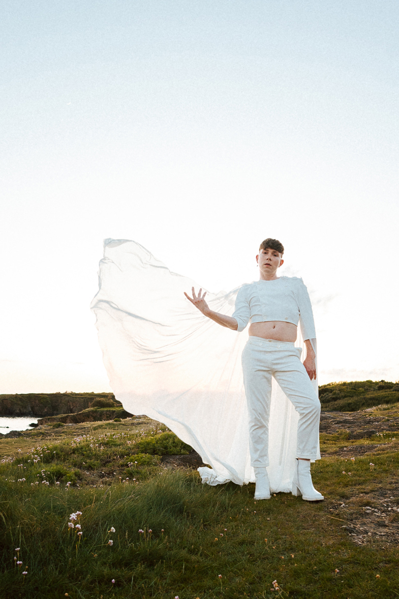 Homme portant un costume de mariage avec une cape en dentelle sur-mesure en bord de mer.