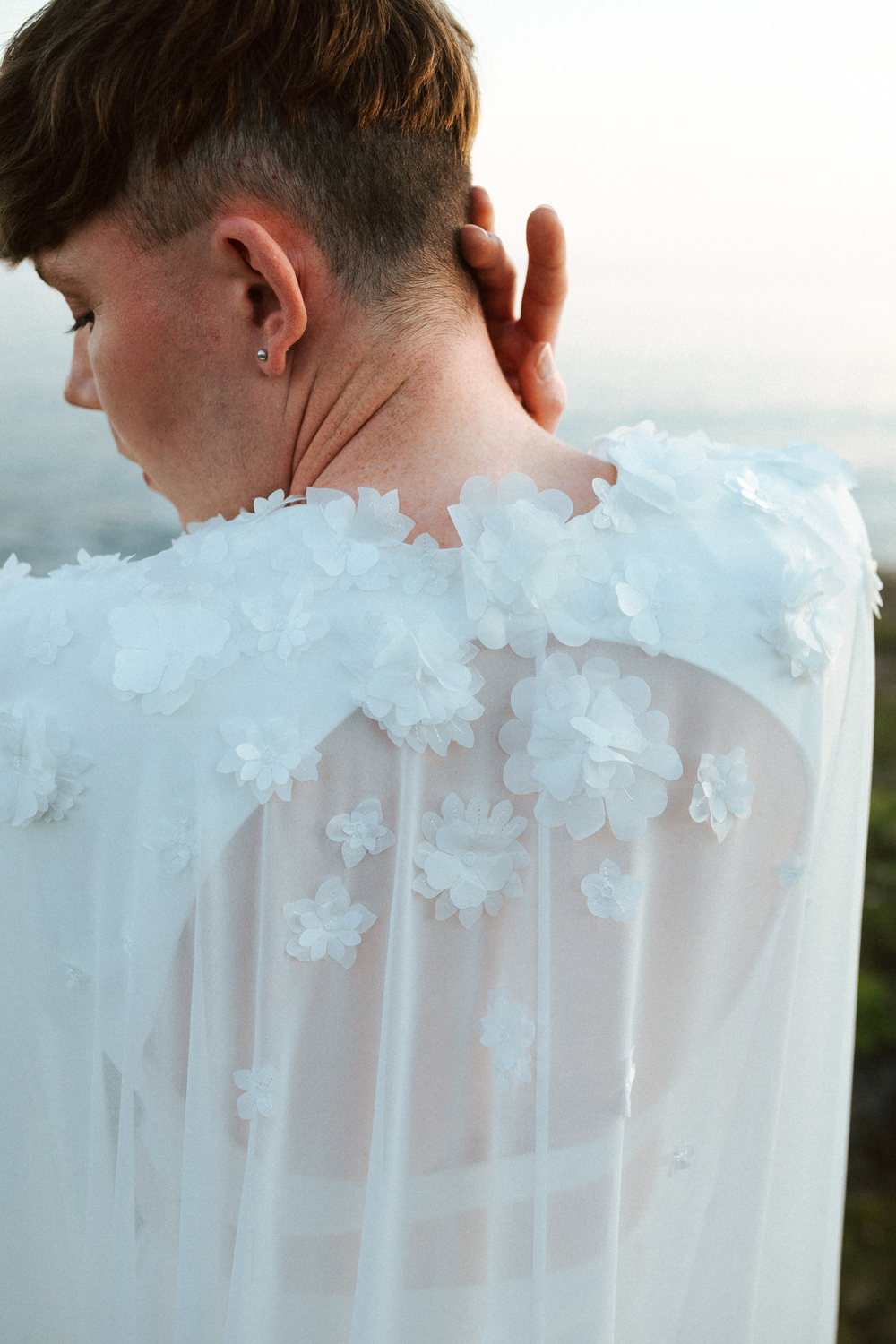 Homme portant un costume de mariage avec une cape en dentelle sur-mesure en bord de mer.