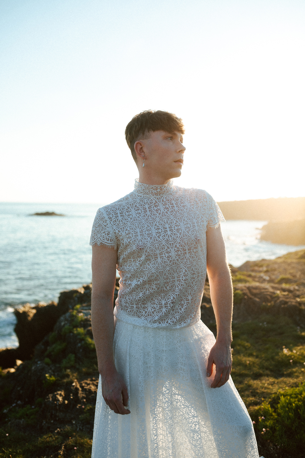 Homme portant un robe de mariage en dentelle sur-mesure en bord de mer.
