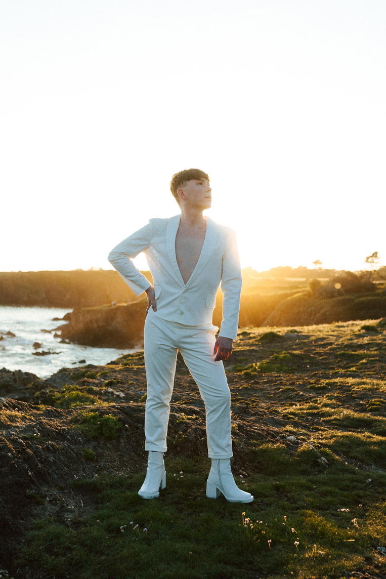 Homme portant un costume de mariage avec un dos nu en dentelle sur-mesure en bord de mer.