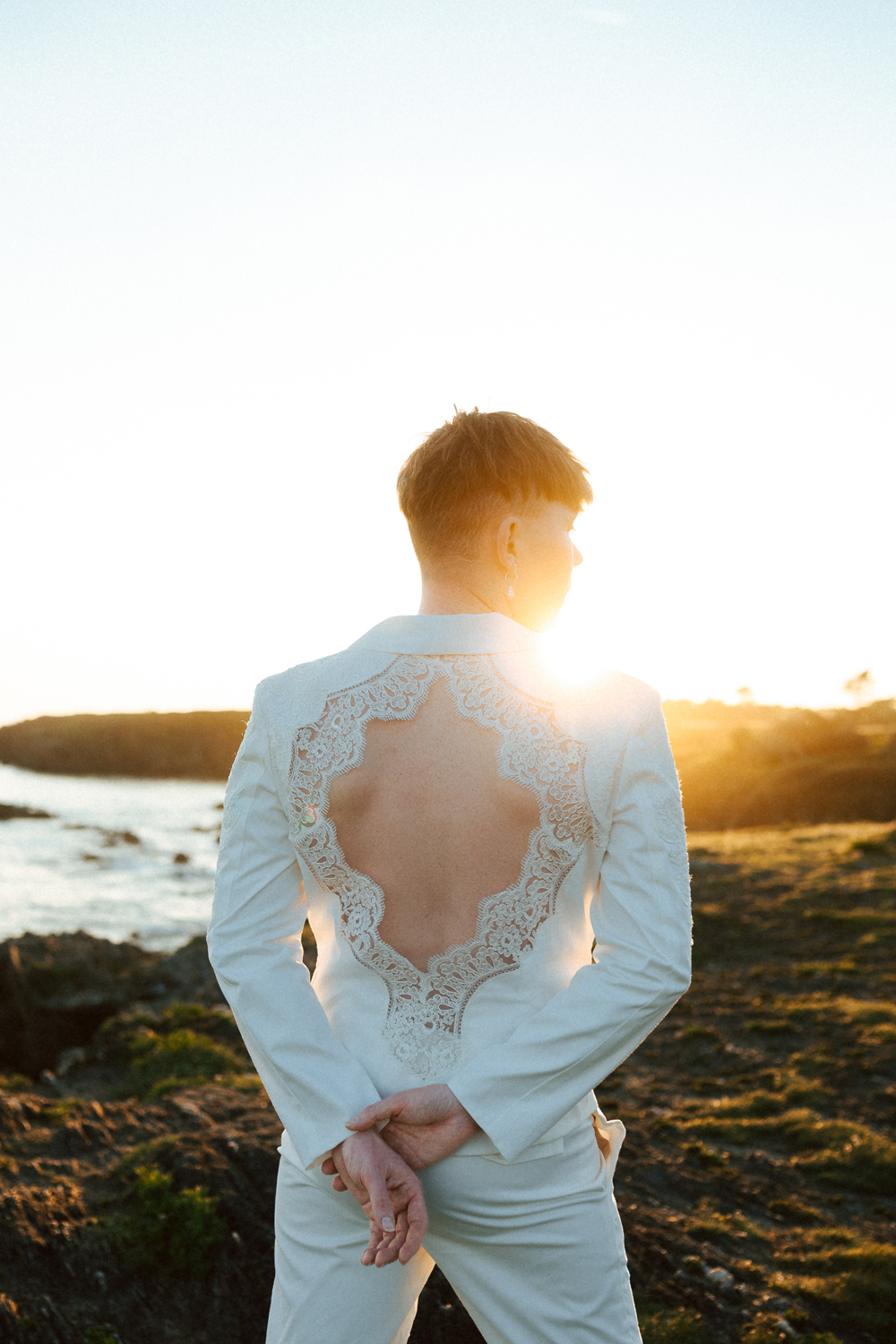 Homme portant un costume de mariage avec un dos nu en dentelle sur-mesure en bord de mer.