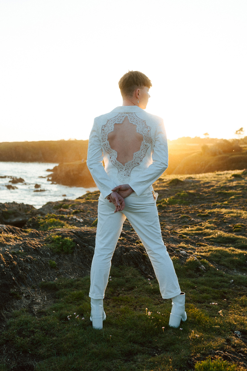 Homme portant un costume de mariage avec un dos nu en dentelle sur-mesure en bord de mer.