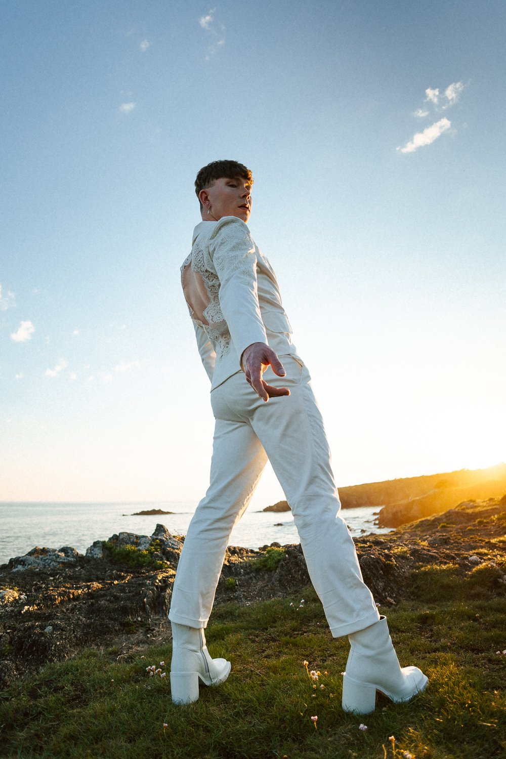 Homme portant un costume de mariage avec un dos nu en dentelle sur-mesure en bord de mer.
