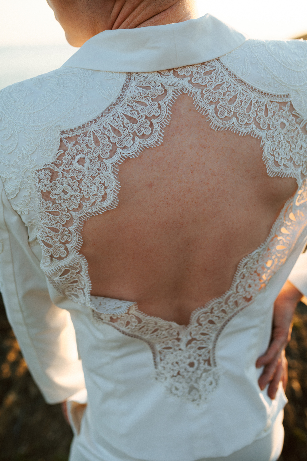 Homme portant un costume de mariage avec un dos nu en dentelle sur-mesure en bord de mer.