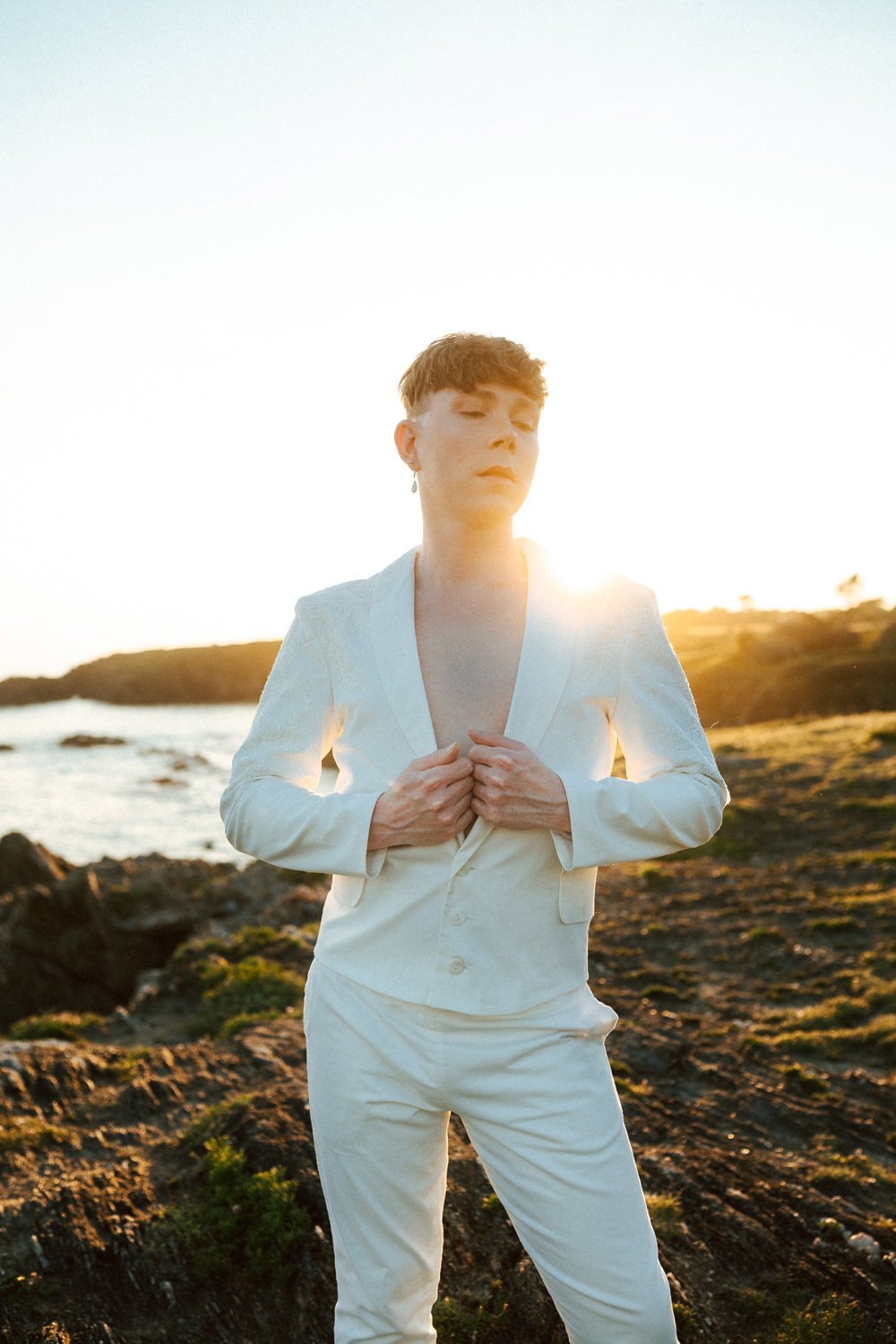 Homme portant un costume de mariage avec un dos nu en dentelle sur-mesure en bord de mer.